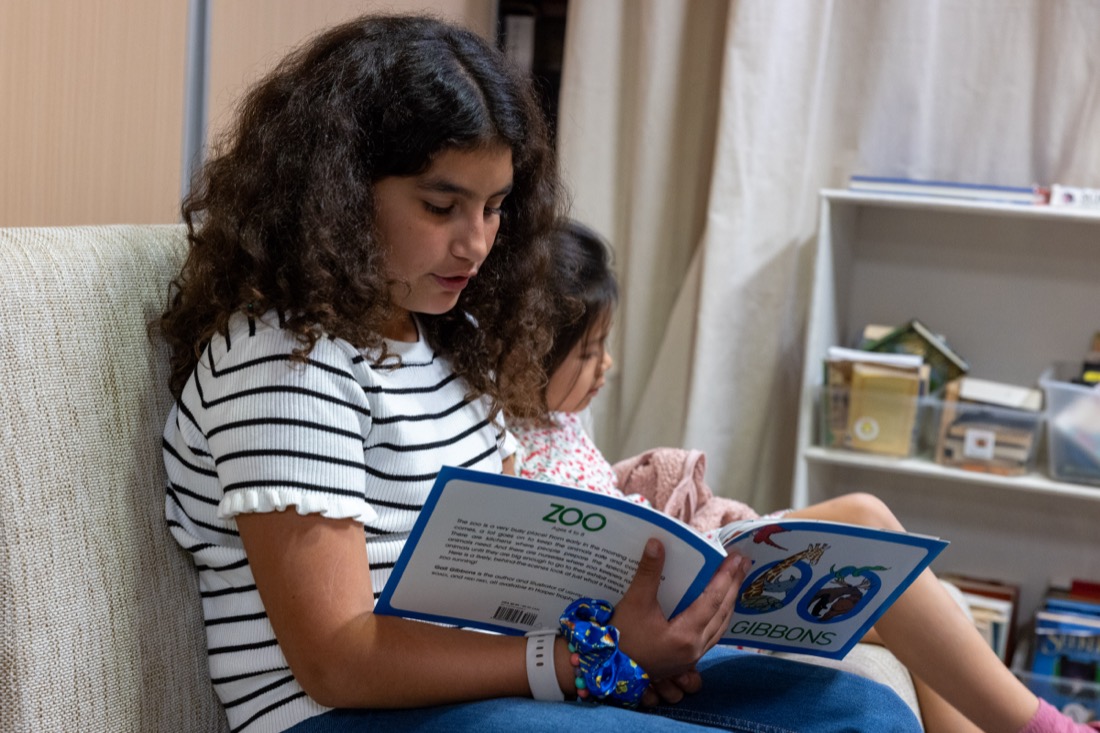 A student reads in one of ASTEME's reading corners, with bookshelves behind her.