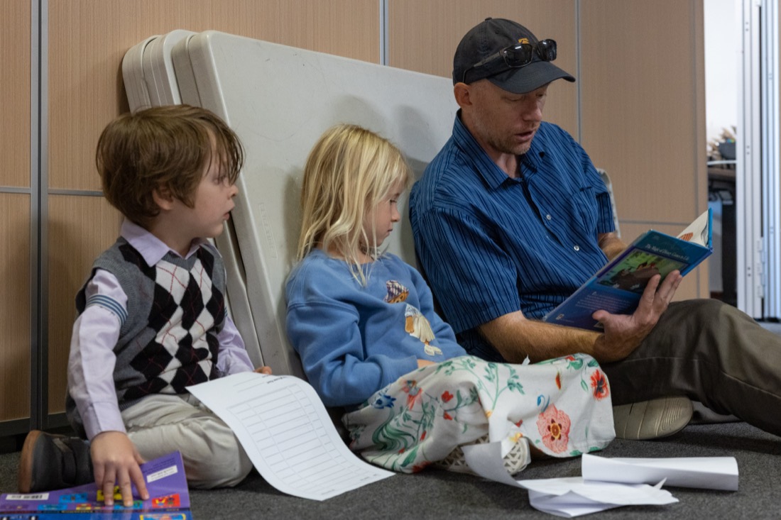 An adult reads a book with two young students on the floor.