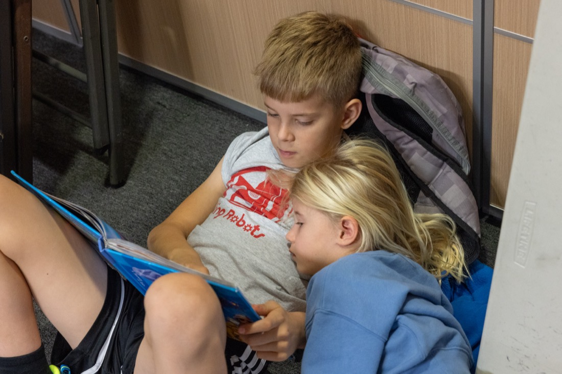 An older student reads to a younger girl who leans on his shoulder.